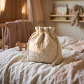 La Pochette de Nuit matelassee en coton creme, posee sur un lit en lin, pour emporter la veilleuse partout - cadeau offert Milo & Lua