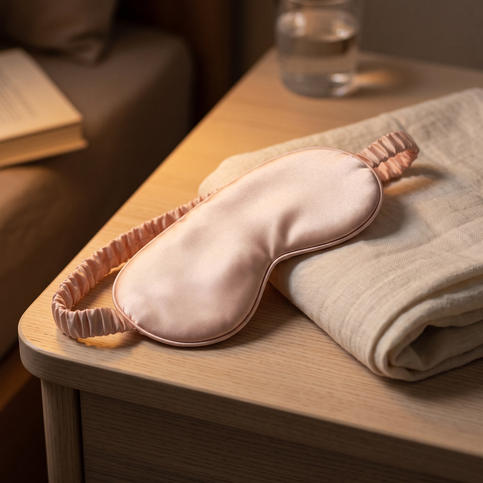Le Masque de Nuit en satin rose poudre pose sur une table de chevet a la lueur d'une veilleuse - cadeau offert Milo & Lua